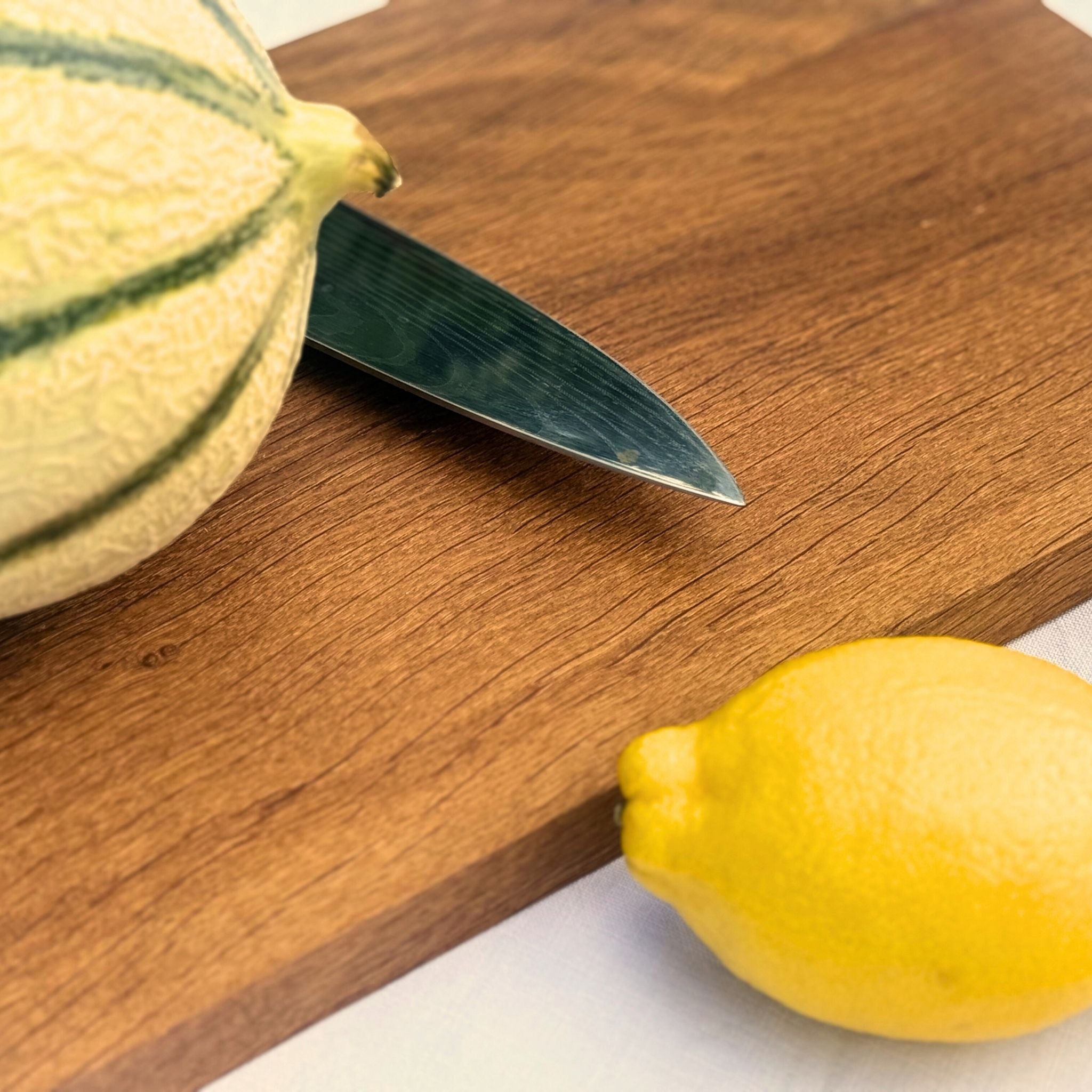 Gros plan sur planche à découper Aiona en chêne, avec couteau, citron et melon.