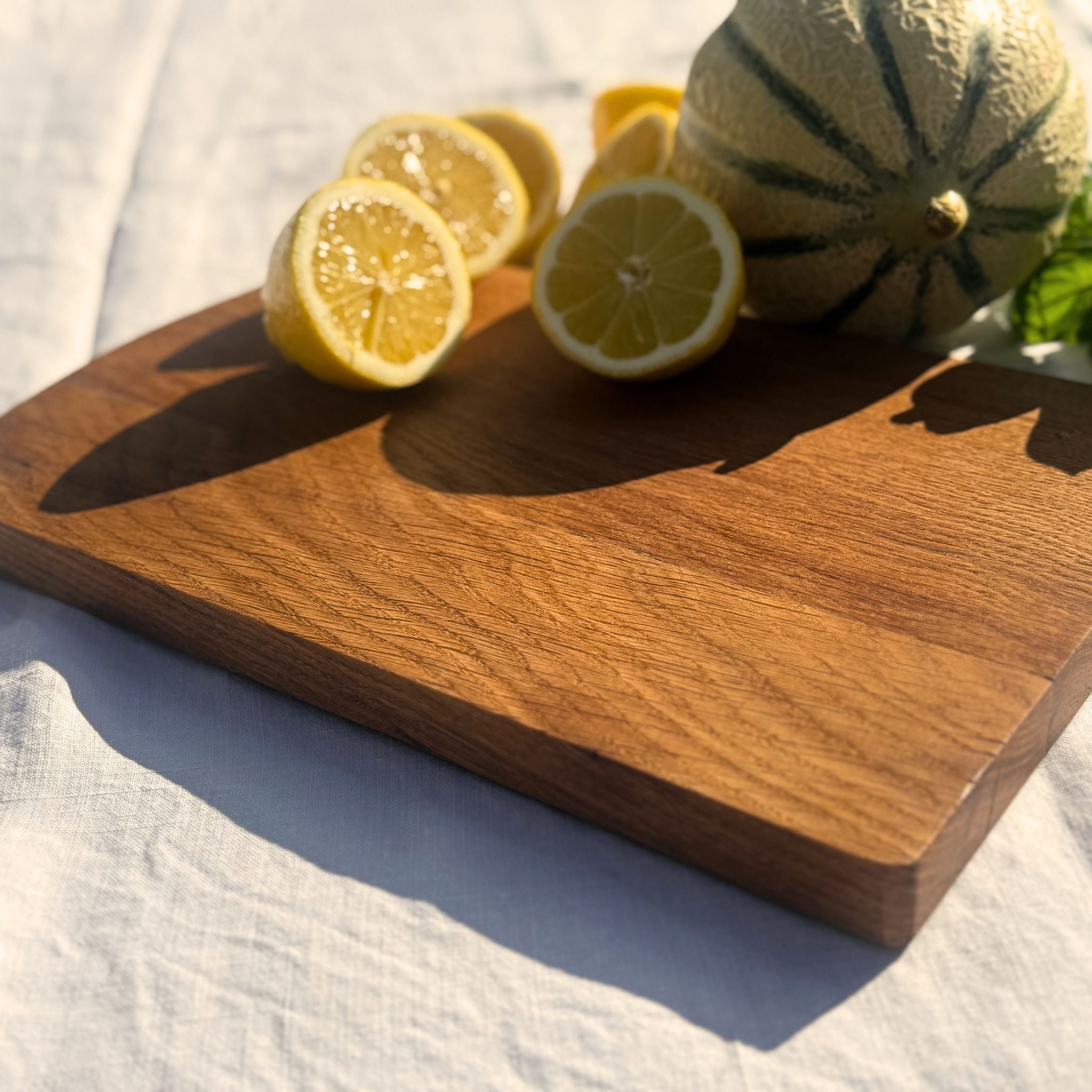 Planche à découper Aiona en chêne massif, vue de biais avec citrons et melon, gros plan sur le veinage du bois.