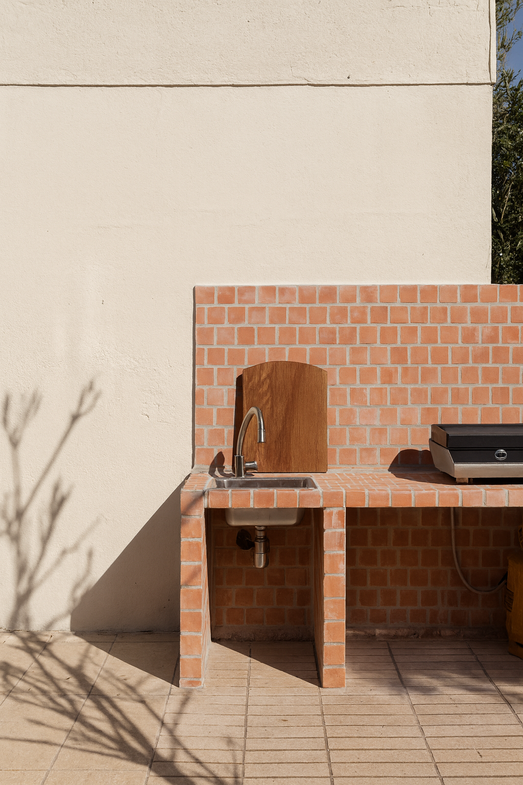 Planche à découper Aiona modèle CAVAILLON en chêne, accrochée sur un mur carrelé terracotta d’une cuisine extérieure avec barbecue.
